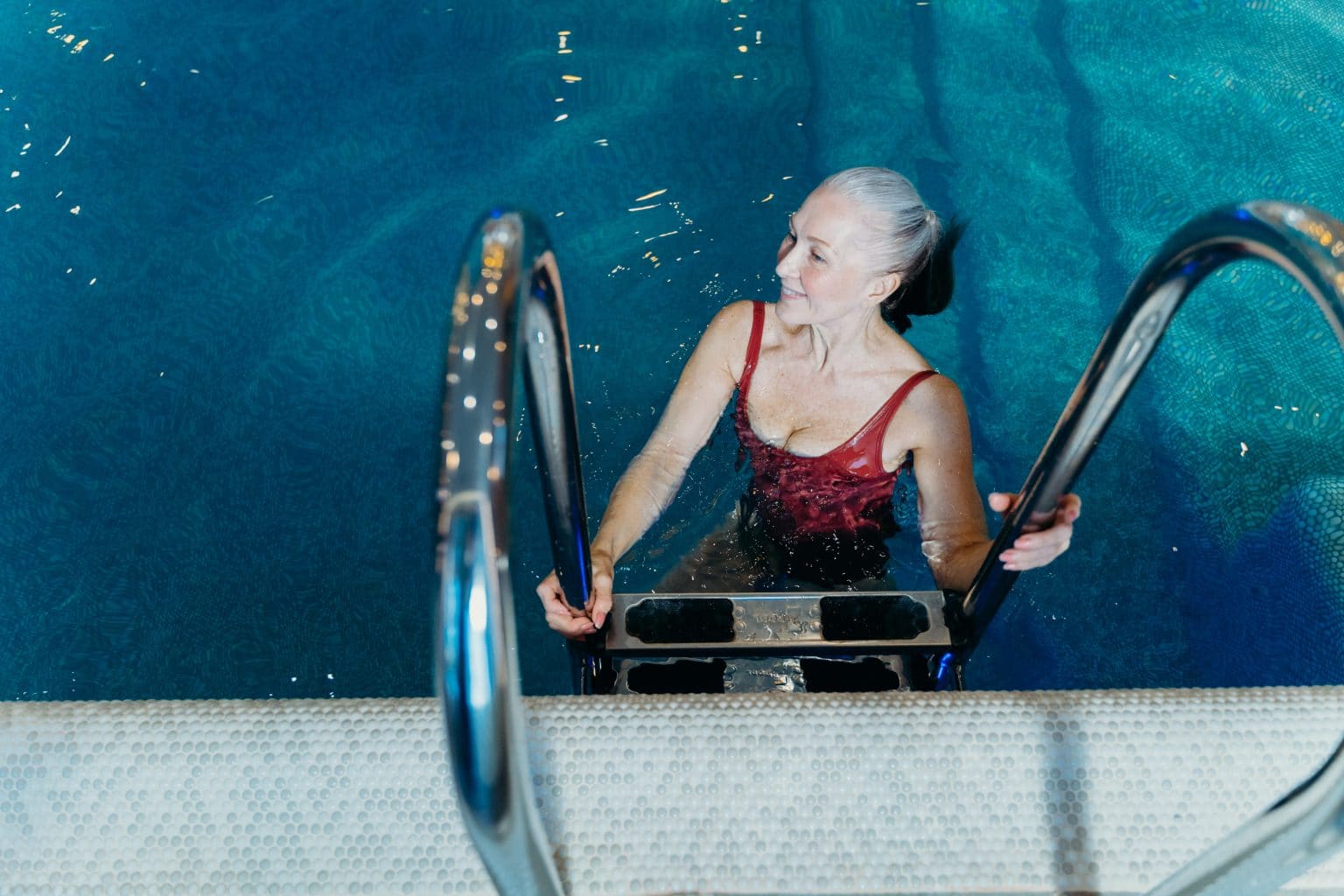 Older woman getting into a swimming pool.