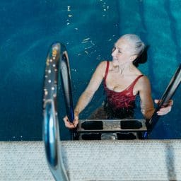 Older woman getting into a swimming pool.