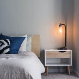 Photo of a bed and a nightstand with a light turned on.