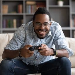 A man smiles as he holds a controller while playing a video game