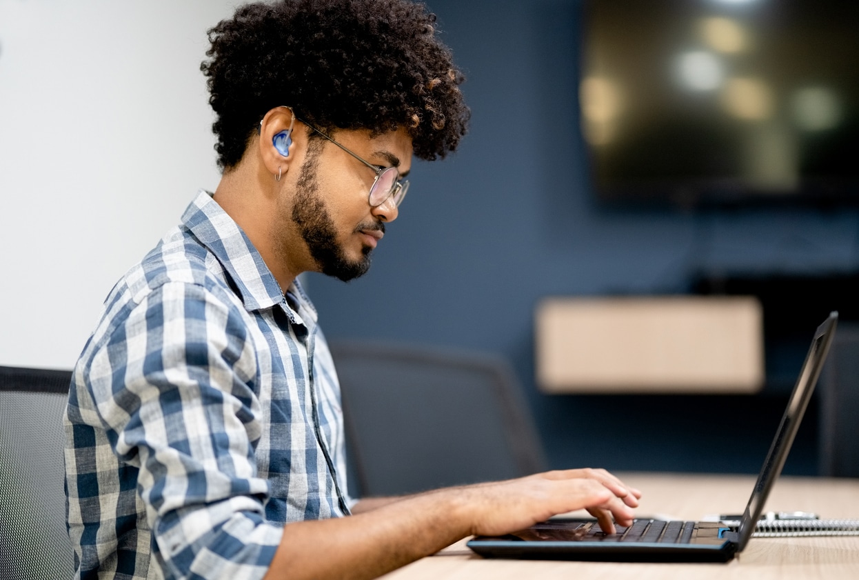 Young man wearing hearing aid sitting at his desk.