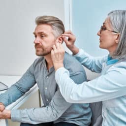 Experienced doctor fitting Intra-The-Ear hearing aid into patient's ear while consultation in audiology clinic. ITE and ITC hearing aids