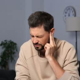 Man holding his ear experiencing tinnitus.