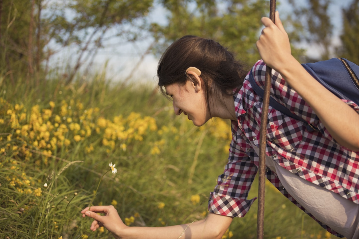 Woman with a hearing aid picking a spring flower.