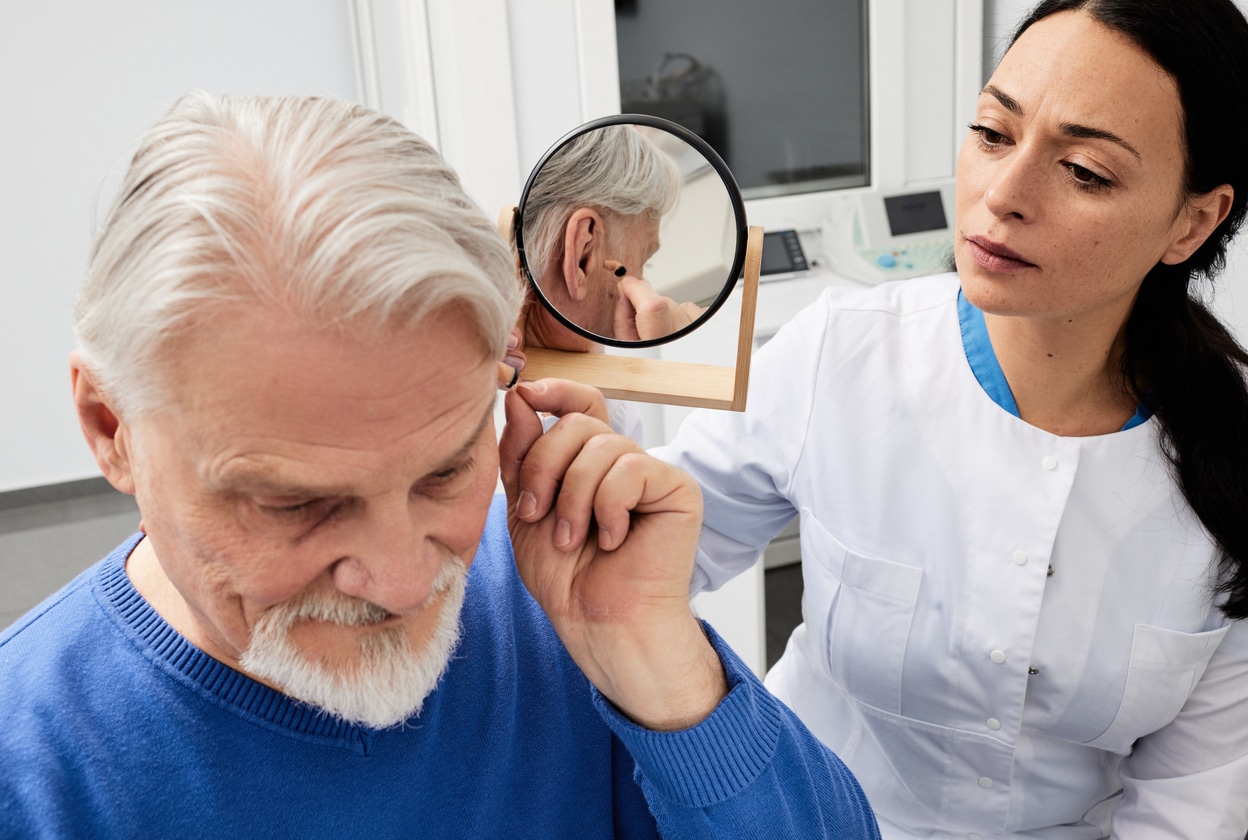 Man adjusts hearing aids with doctor