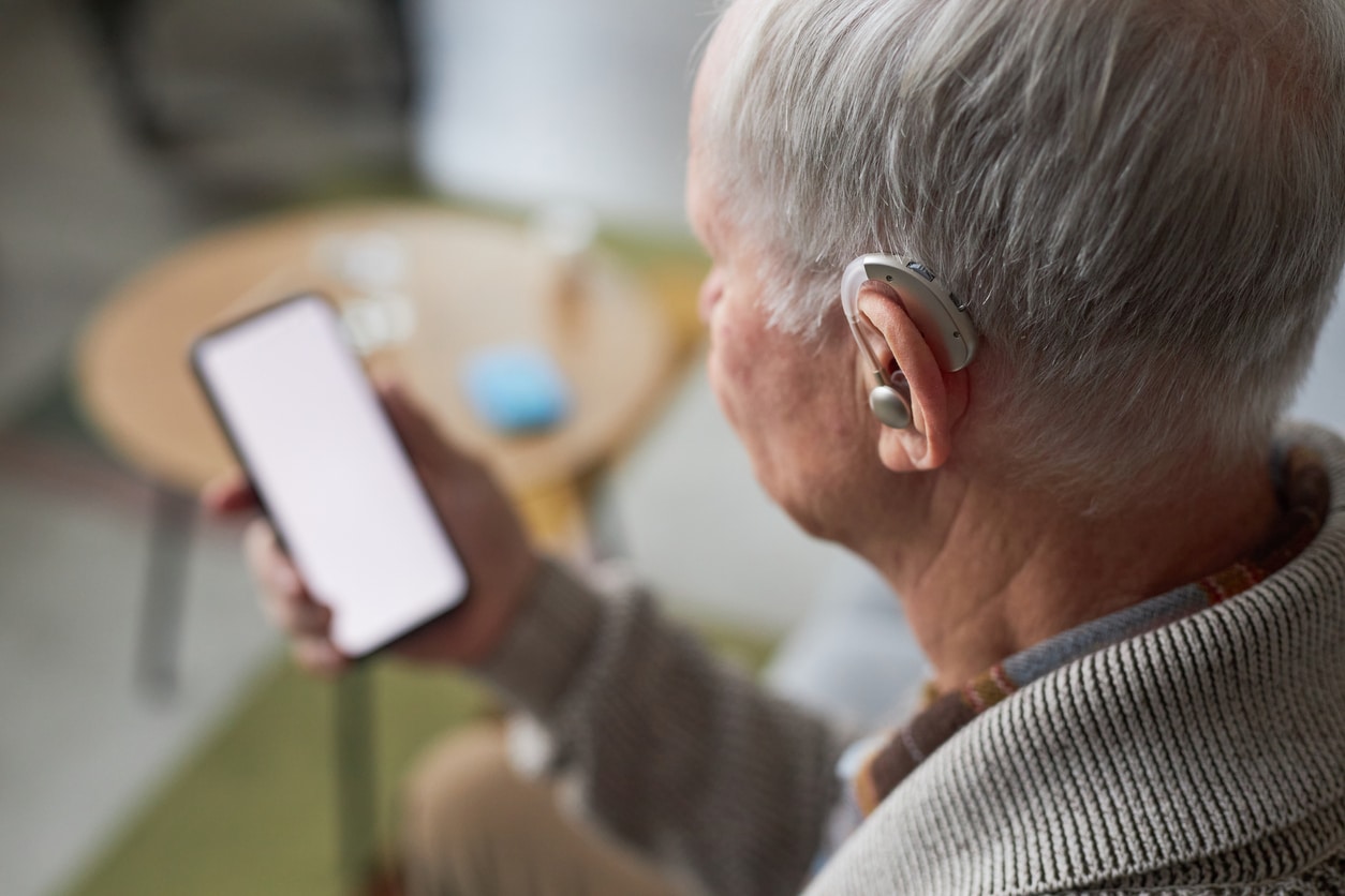 Man with hearing aids looks at his phone