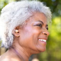 Senior woman wearing a hearing aid in the park, looking happy