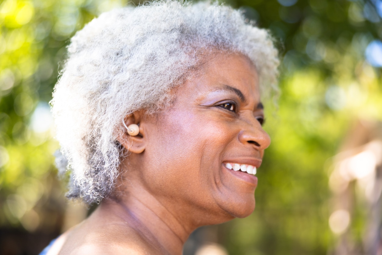 Senior woman wearing a hearing aid in the park, looking happy.