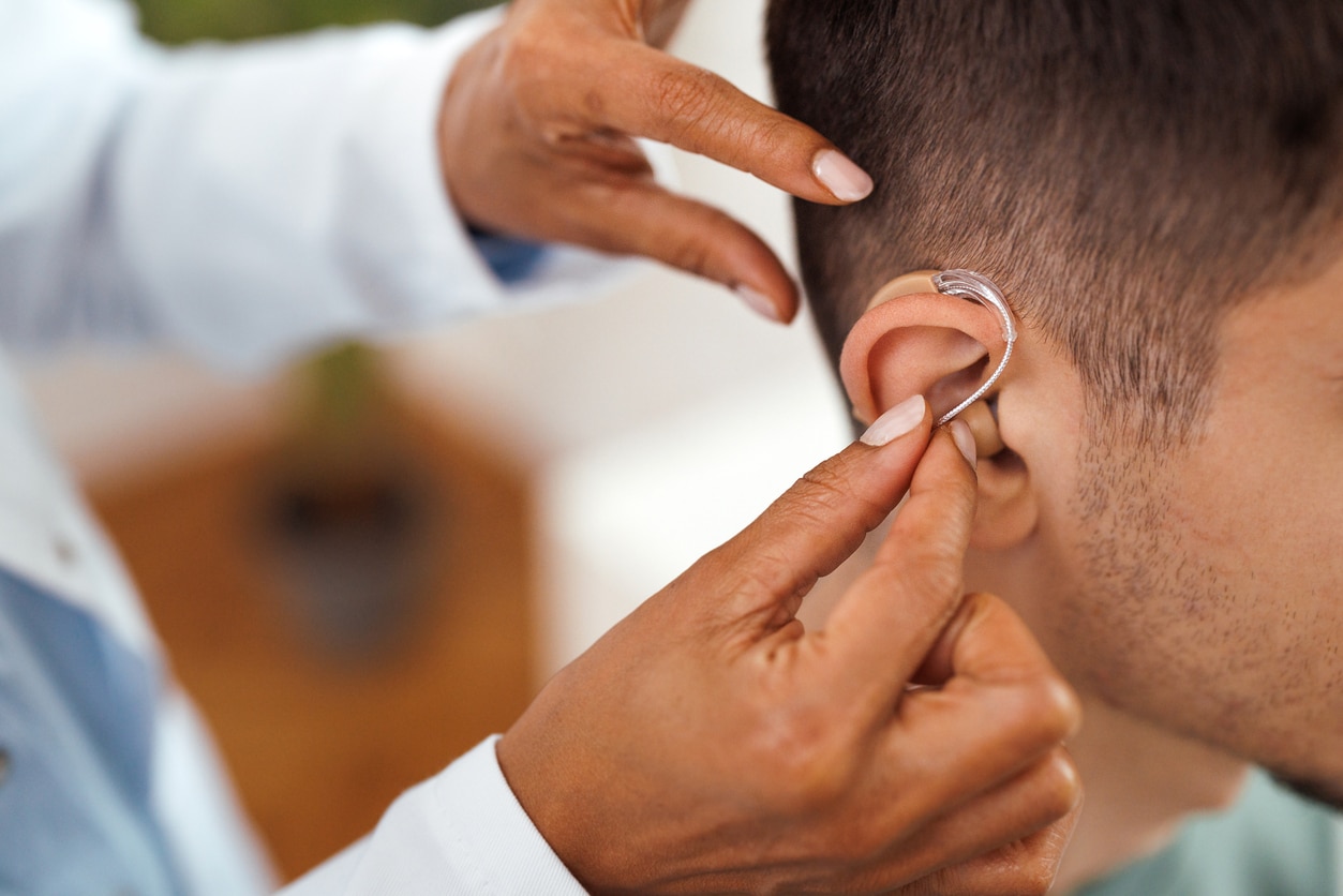 Audiologist putting a hearing aid on a patient.